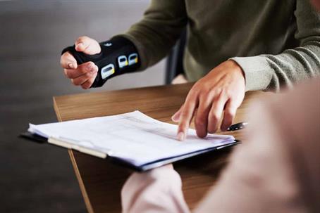 A client with an injured hand is checking a document held out by a lawyer.